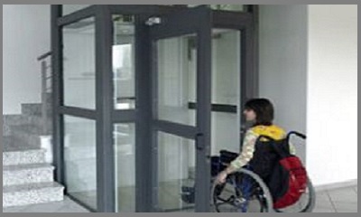 Una persona in carrozzina davanti ad un ascensore accessibile anche per i disabili