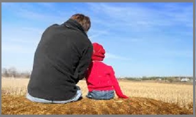 padre e figlia piccina seduti su un campo di paglia presi da dietro guardano all'orizzonte